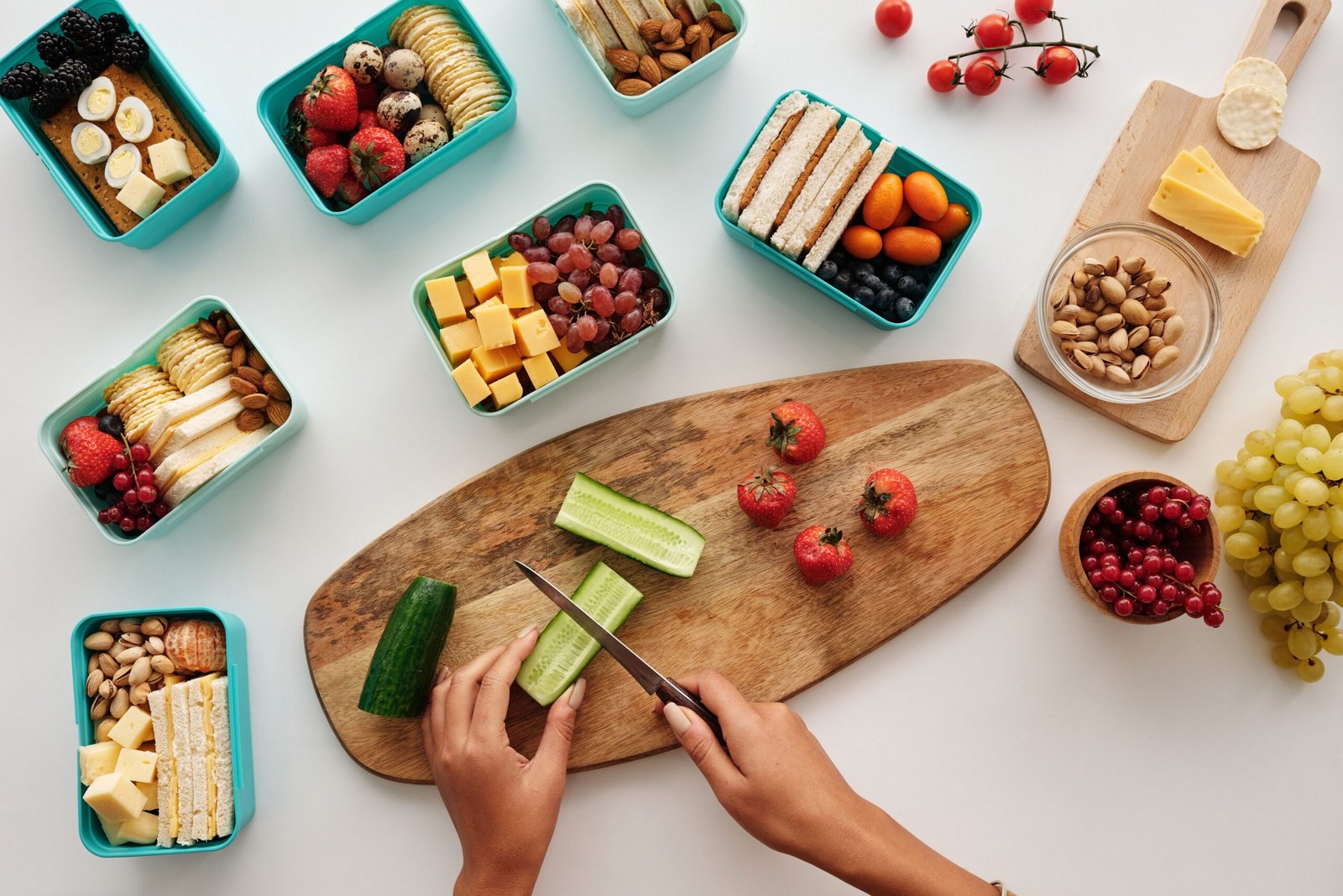 tabua de madeira e mãos a cortar frutas e legumes para preparar a lancheira escolar